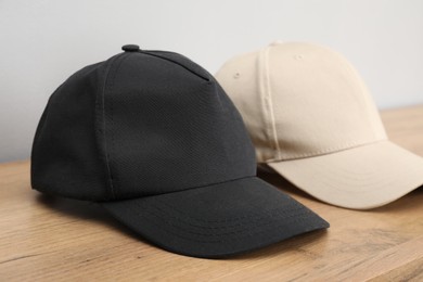 Photo of Stylish baseball caps on wooden table, closeup. Mockup for design