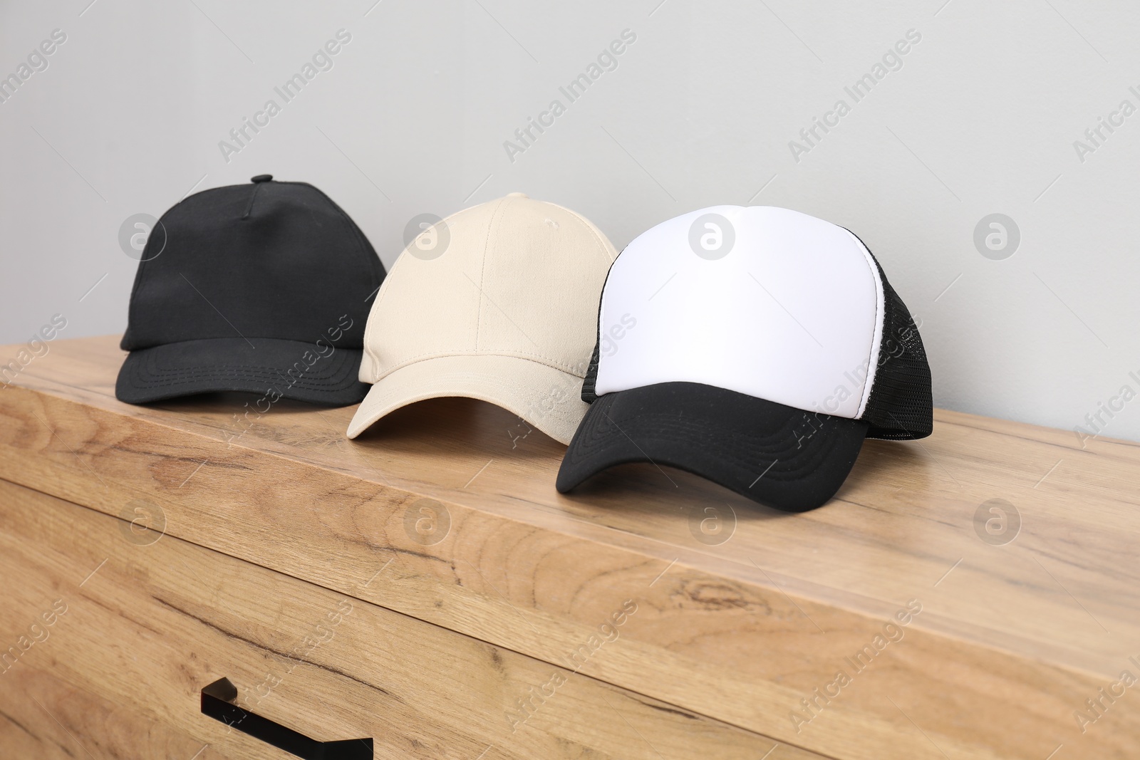 Photo of Stylish baseball caps on wooden chest of drawers. Mockup for design