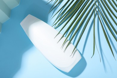 Photo of Shampoo in bottle and palm leaf on light blue background, top view