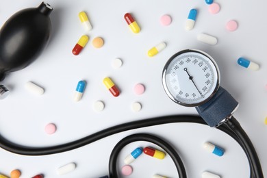 Photo of Blood pressure measuring device and pills on white background, flat lay