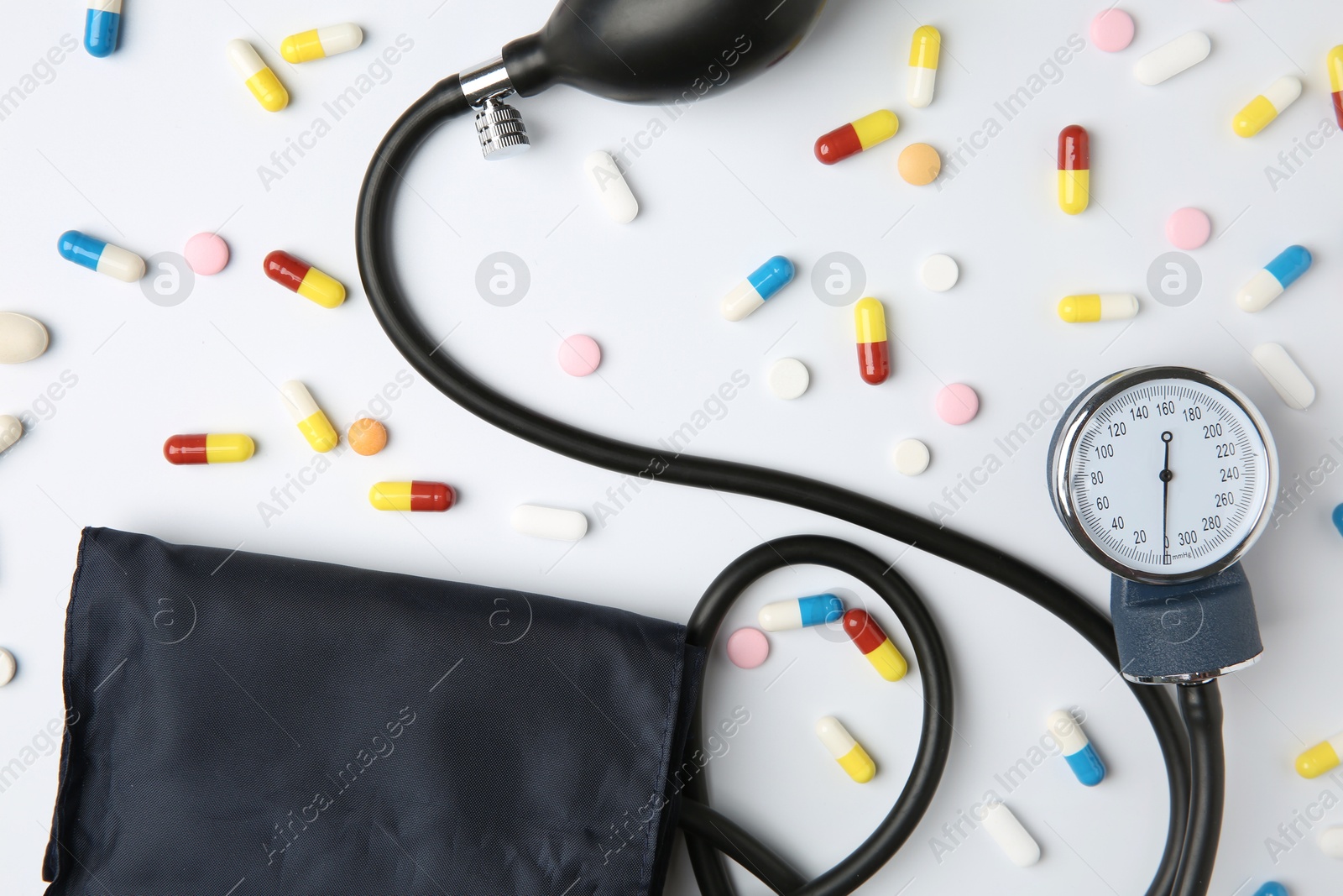 Photo of Blood pressure measuring device and pills on white background, flat lay