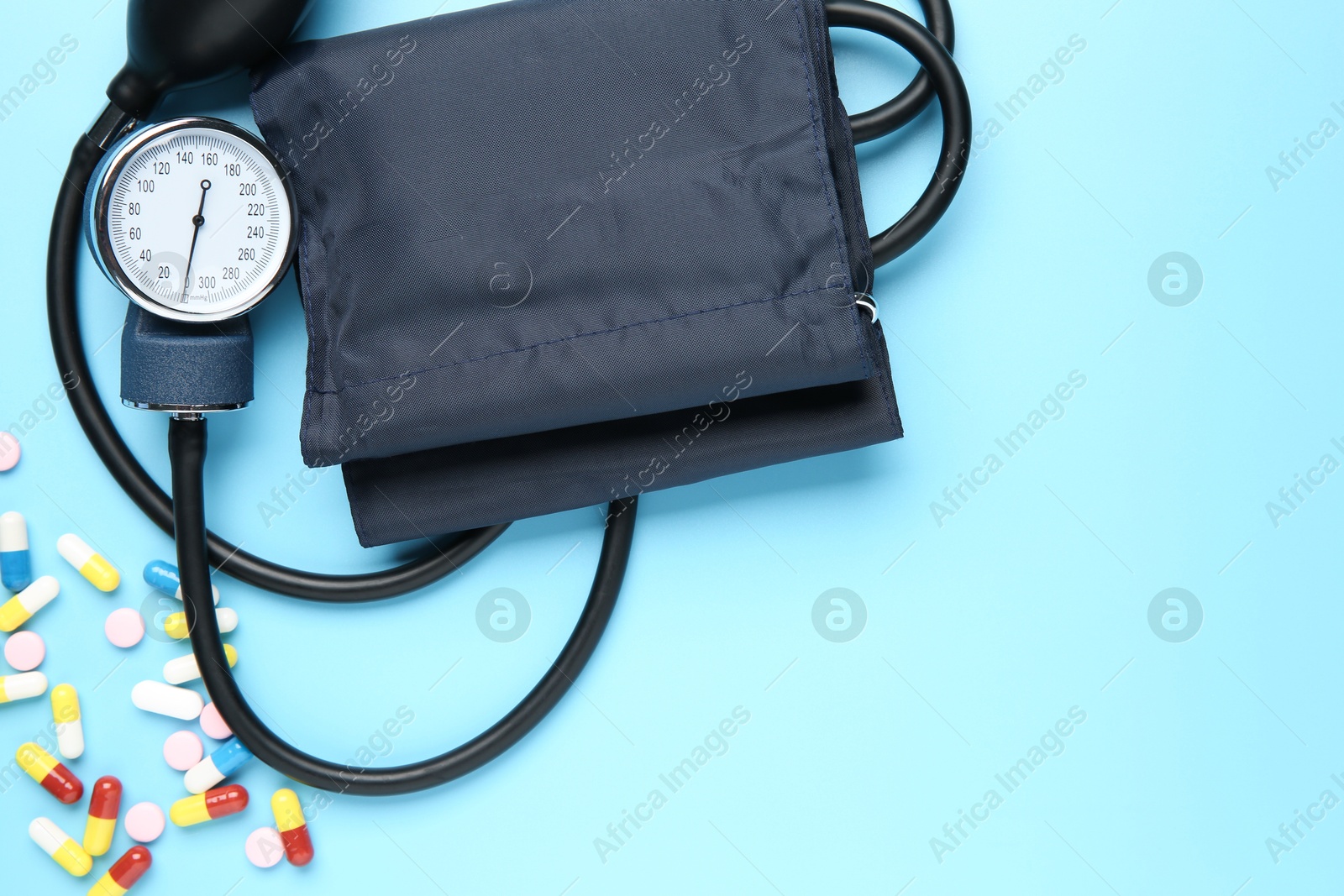 Photo of Blood pressure measuring device and pills on light blue background, top view. Space for text