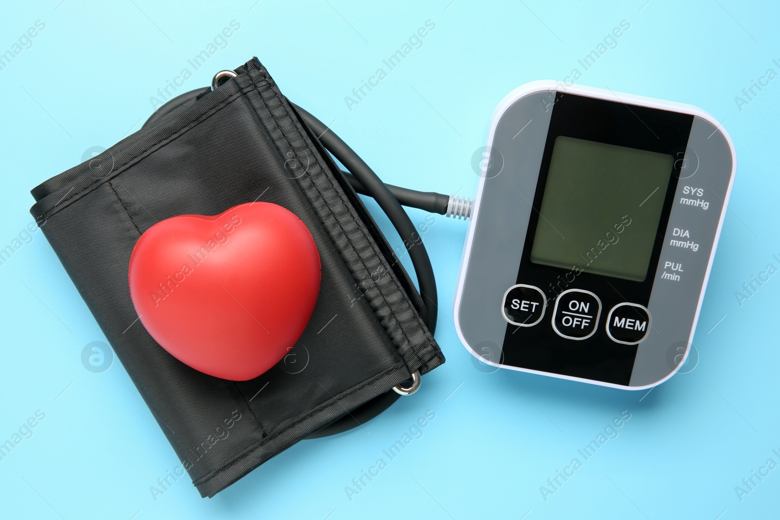 Photo of Blood pressure measuring device and squeeze heart on light blue background, top view