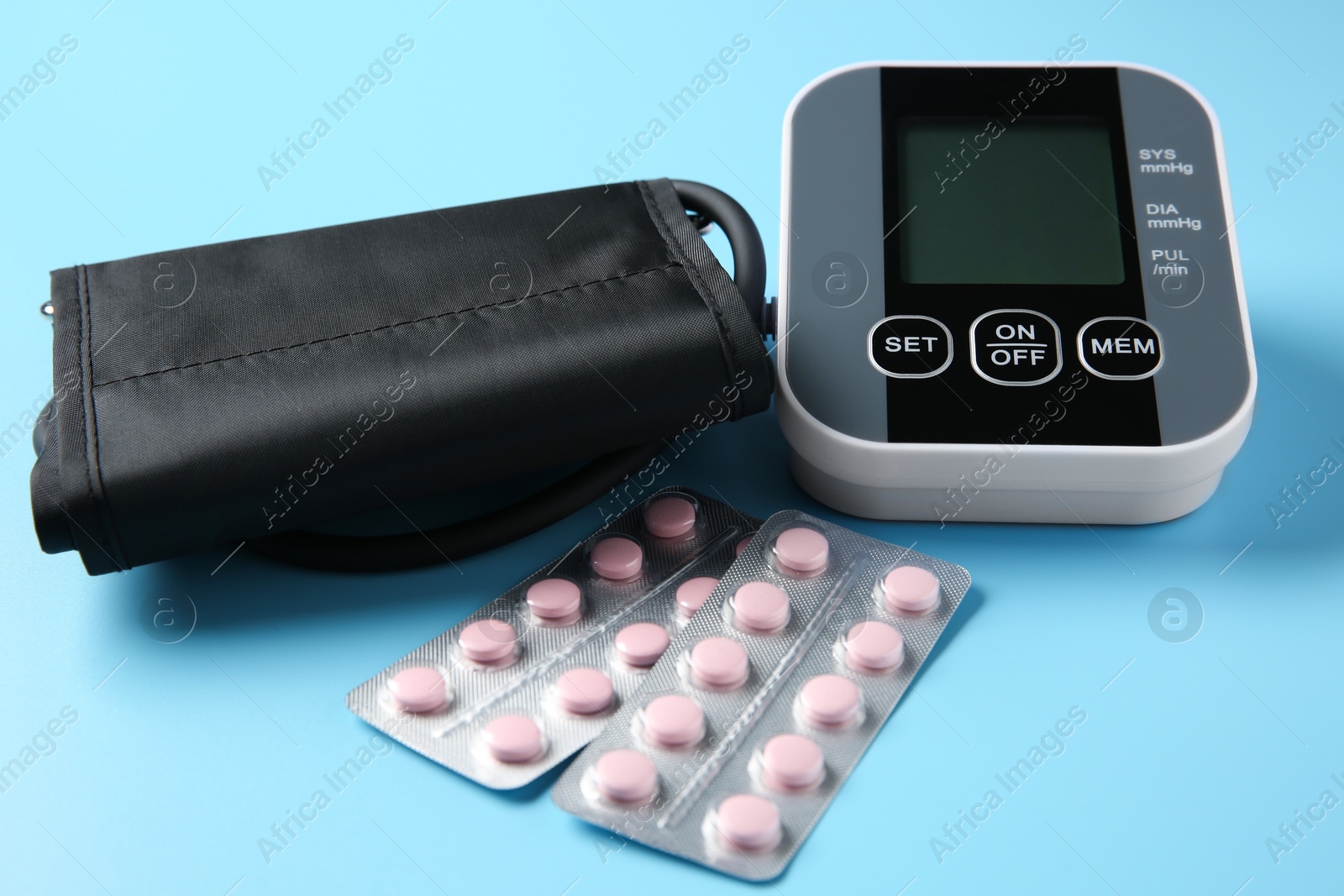 Photo of Blood pressure measuring device and pills on light blue background, closeup