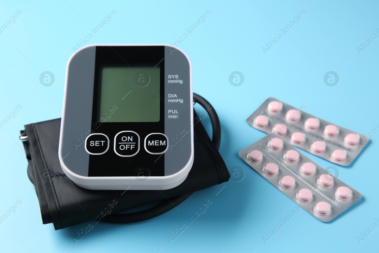 Photo of Blood pressure measuring device and pills on light blue background, closeup