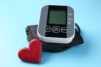 Photo of Blood pressure measuring device and heart figure on light blue background, closeup