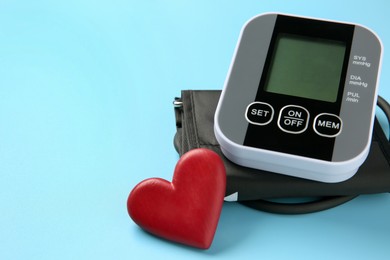 Blood pressure measuring device and heart figure on light blue background, closeup. Space for text