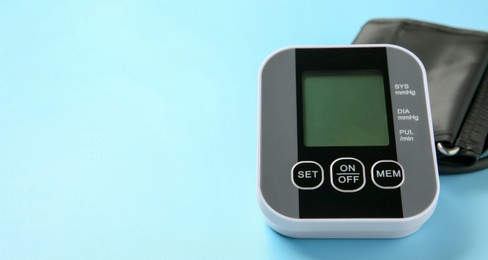 Blood pressure measuring device on light blue background, closeup. Space for text