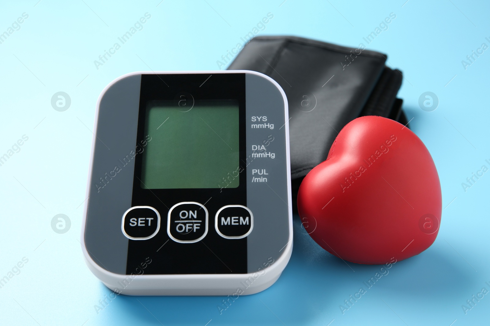 Photo of Blood pressure measuring device and squeeze heart on light blue background, closeup