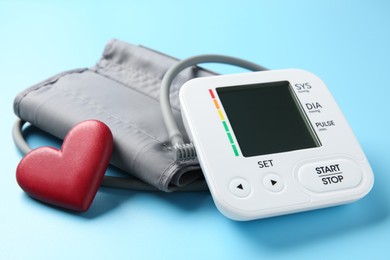 Photo of Blood pressure measuring device and heart figure on light blue background, closeup