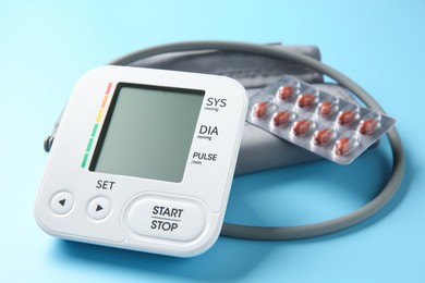 Blood pressure measuring device and pills on light blue background, closeup