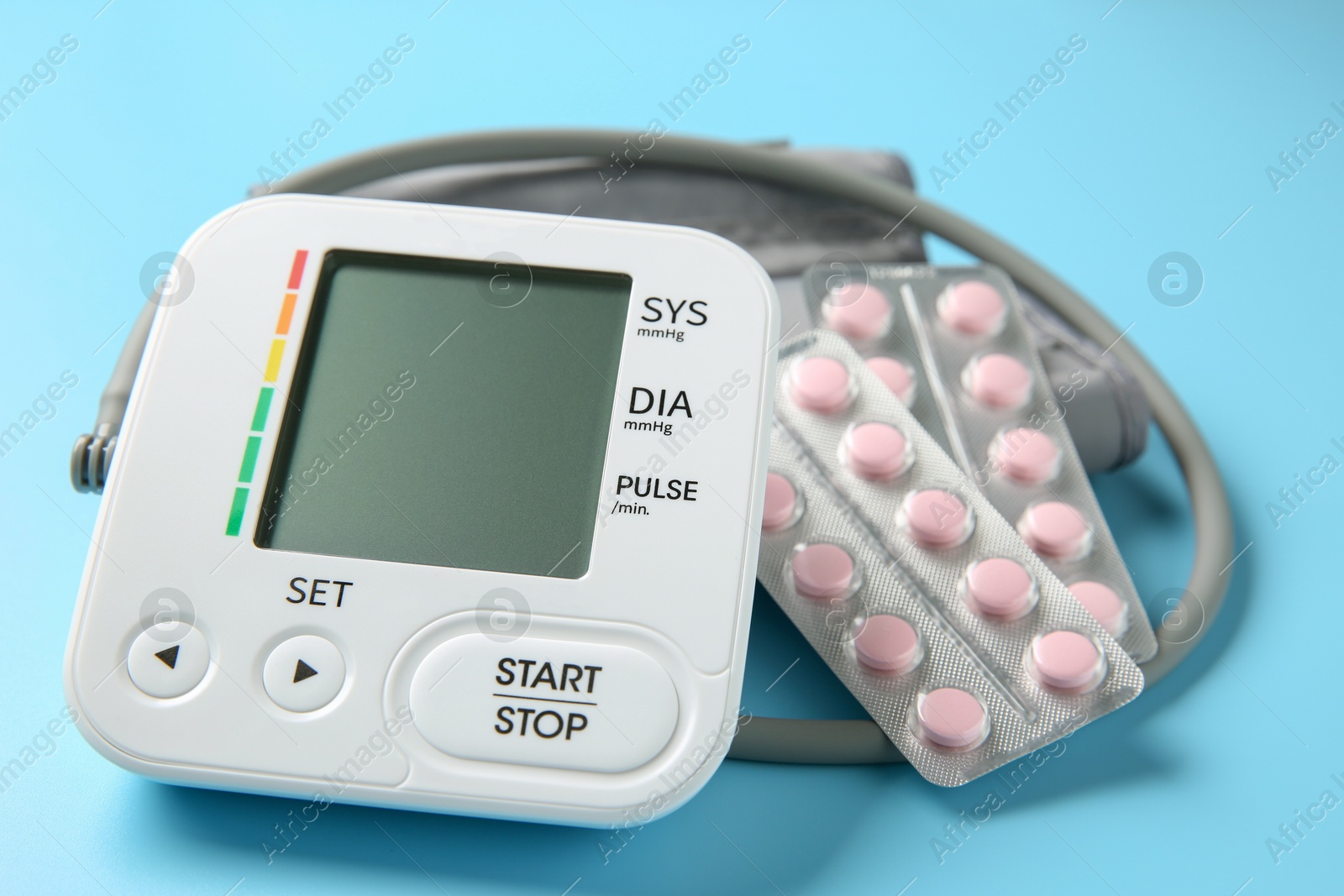 Photo of Blood pressure measuring device and pills on light blue background, closeup