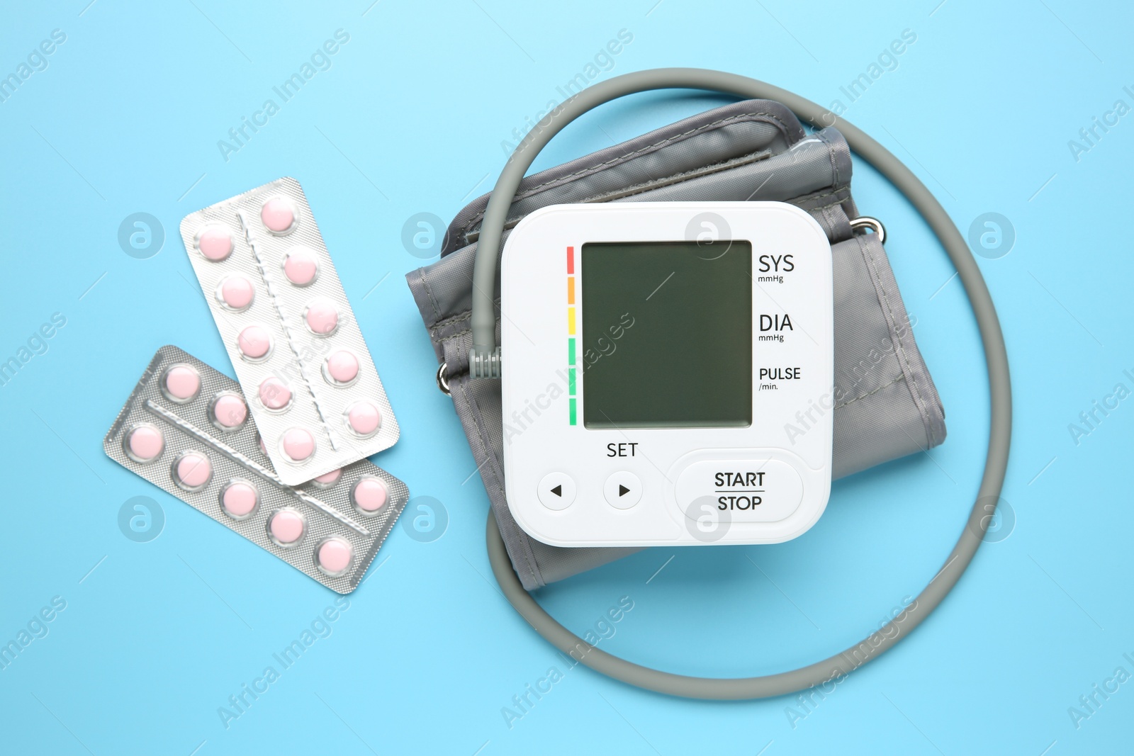 Photo of Blood pressure measuring device and pills on light blue background, top view