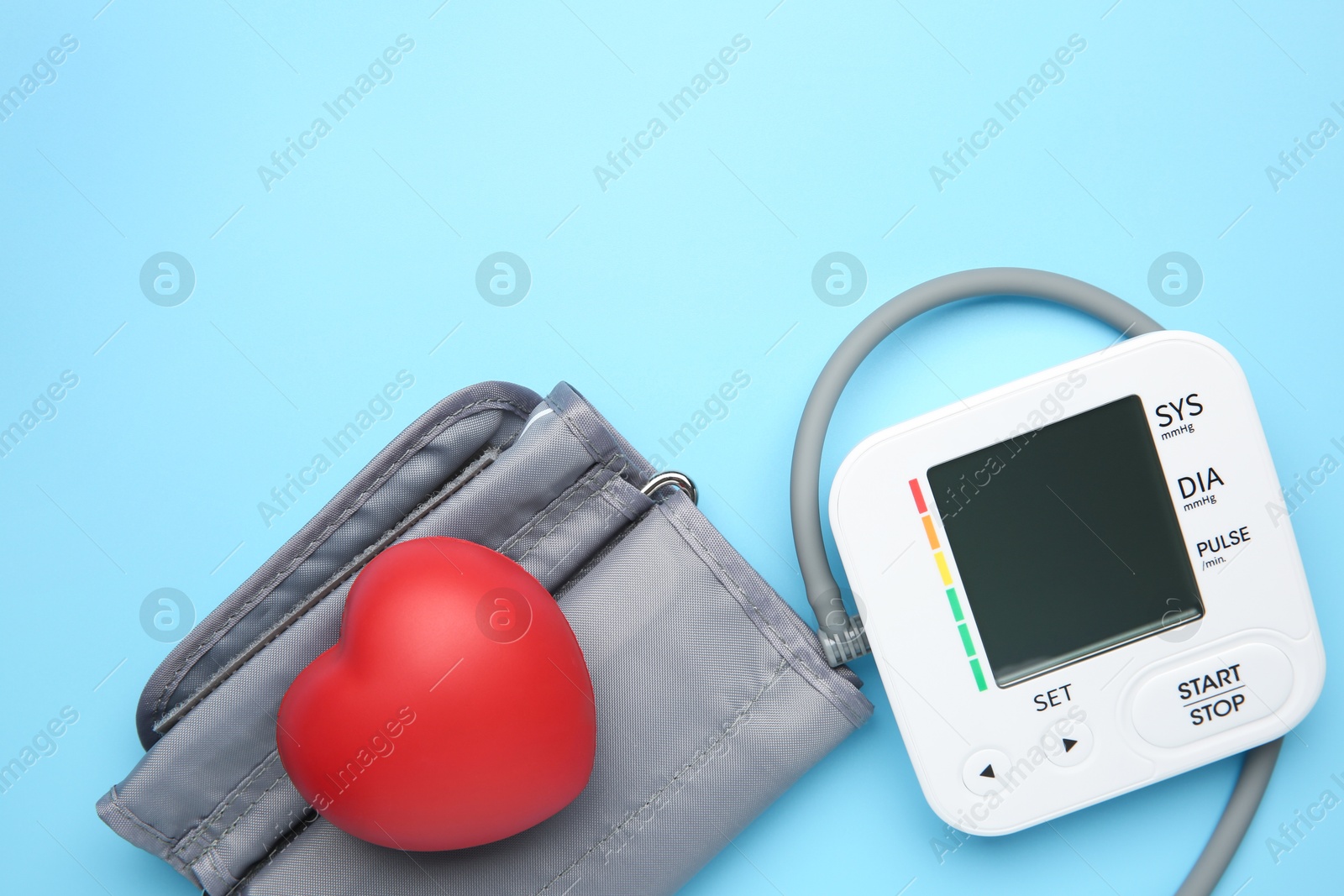 Photo of Blood pressure measuring device and squeeze heart on light blue background, top view