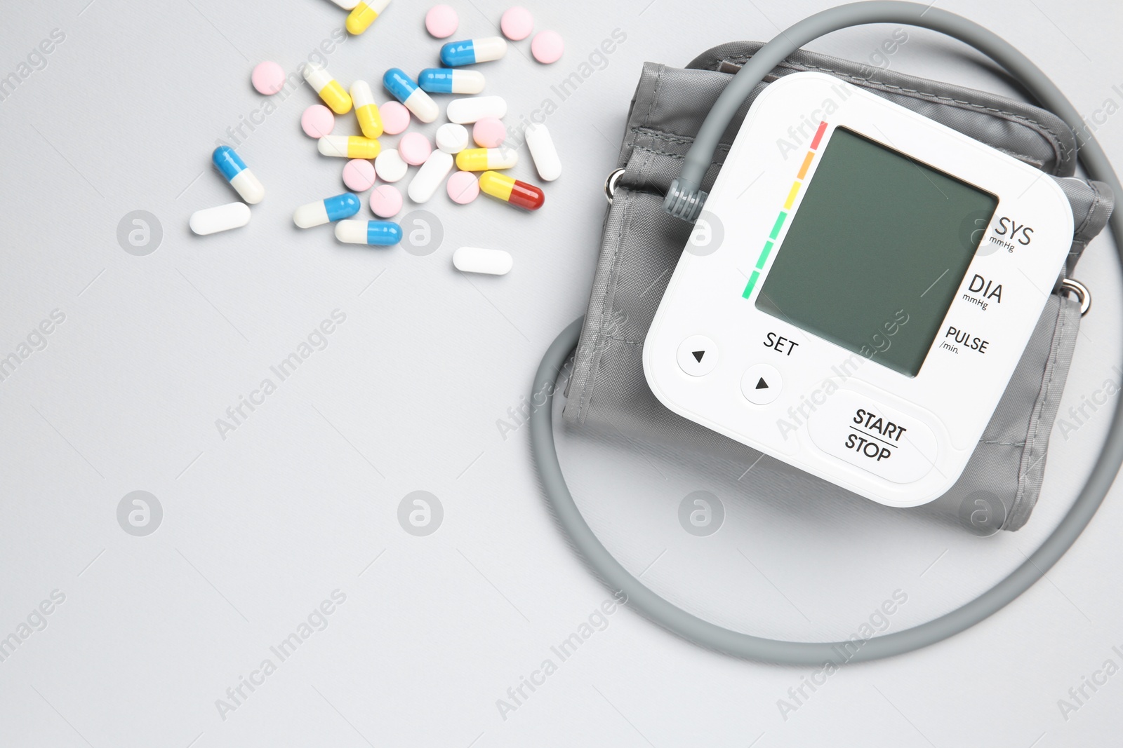 Photo of Blood pressure measuring device and pills on light grey background, top view. Space for text