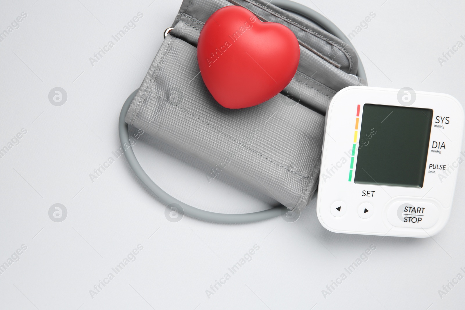 Photo of Blood pressure measuring device and squeeze heart on light grey background, top view