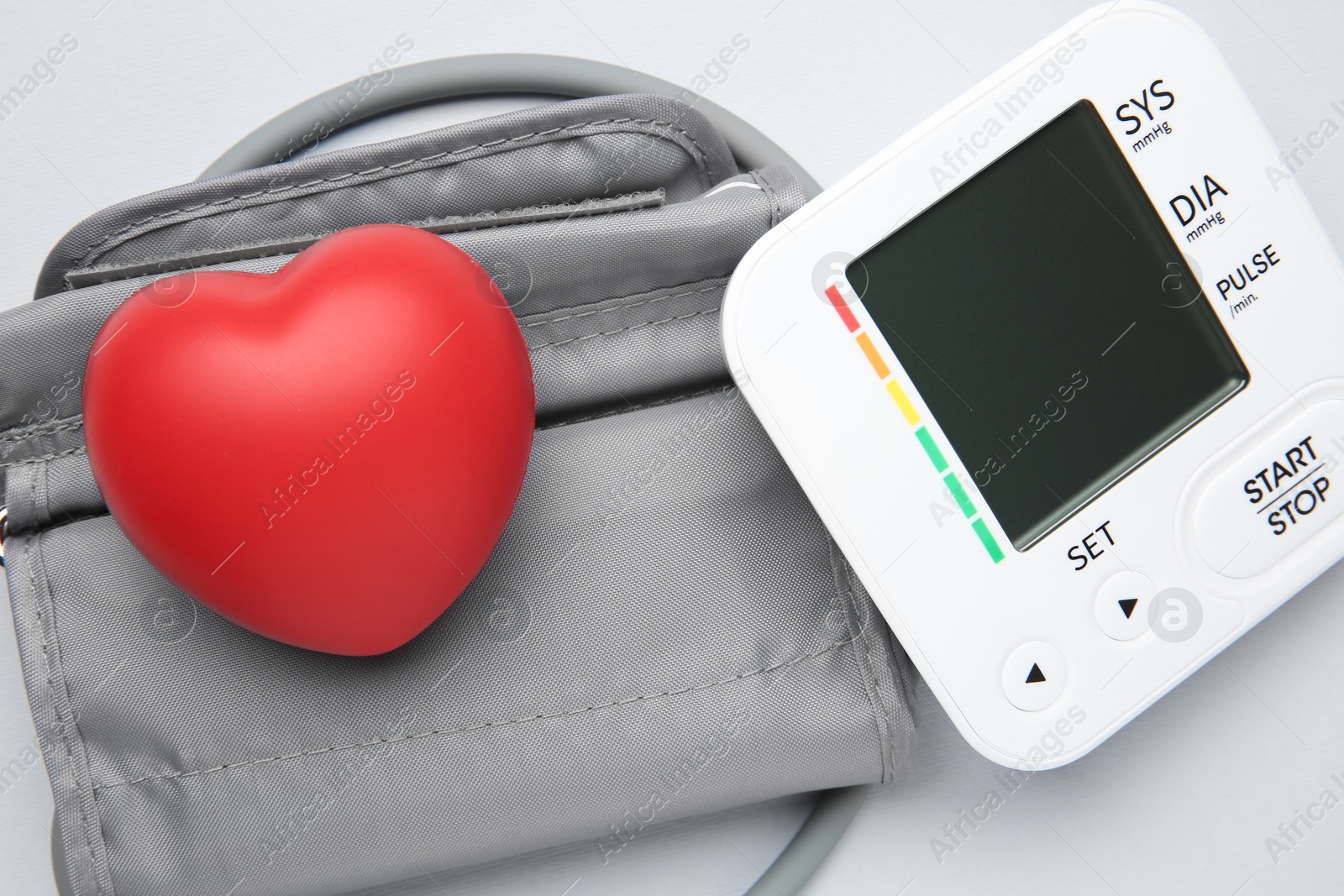 Photo of Blood pressure measuring device and squeeze heart on light grey background, top view