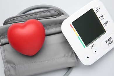 Blood pressure measuring device and squeeze heart on light grey background, top view