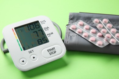 Photo of Blood pressure measuring device and pills on green background, closeup