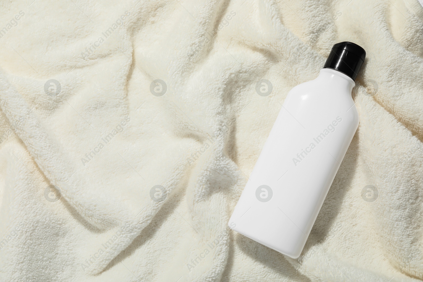 Photo of Shampoo in bottle on soft towel, top view. Space for text