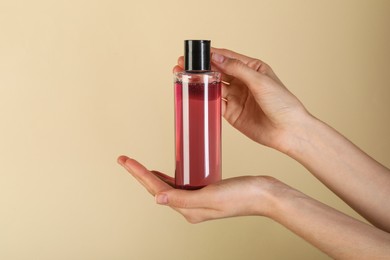 Photo of Woman with shampoo bottle on beige background, closeup