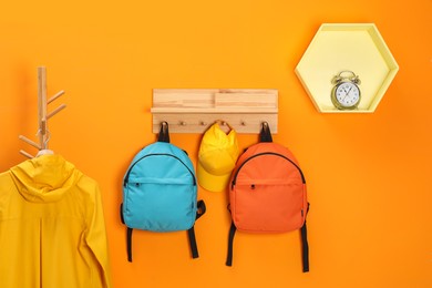 Photo of Bright backpacks, cap, coat and alarm clock near orange wall