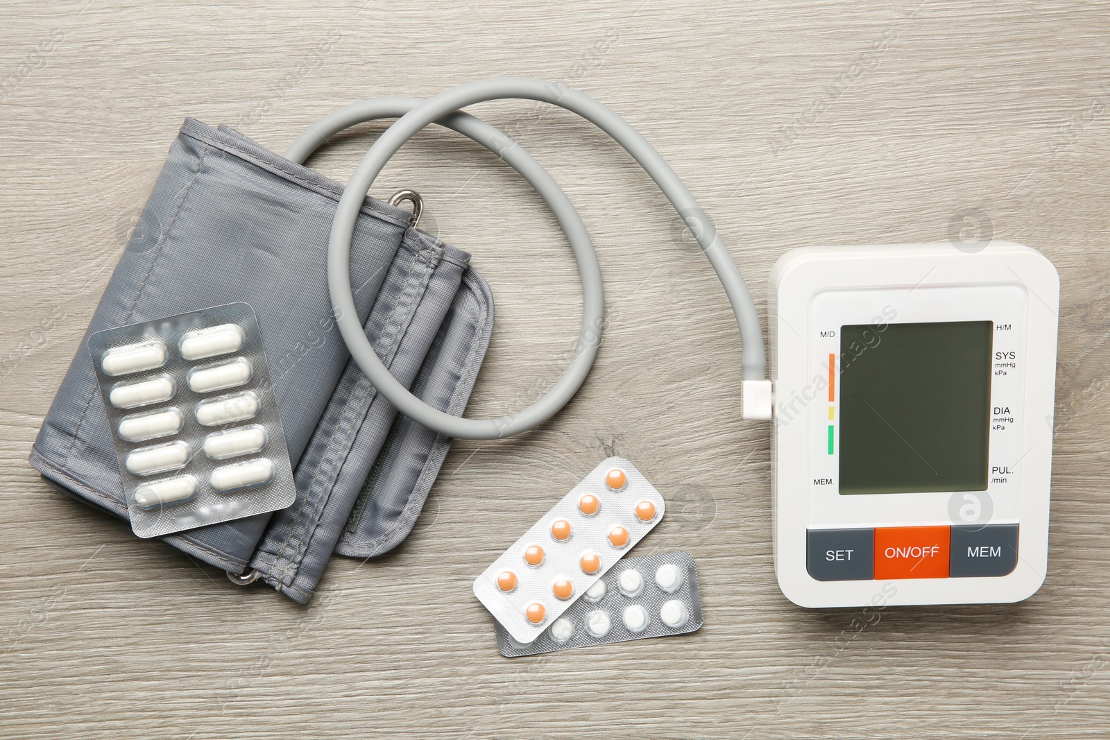 Photo of Blood pressure measuring device and pills on wooden table, flat lay