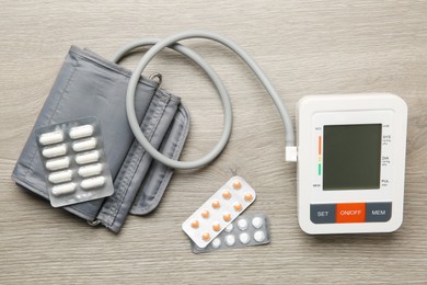 Blood pressure measuring device and pills on wooden table, flat lay