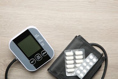 Photo of Blood pressure measuring device and pills on wooden table, top view