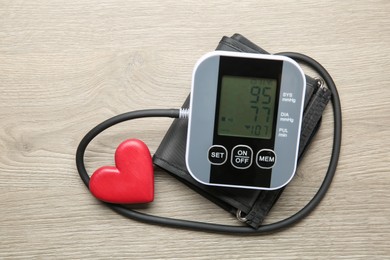 Photo of Blood pressure measuring device and heart figure on wooden table, top view