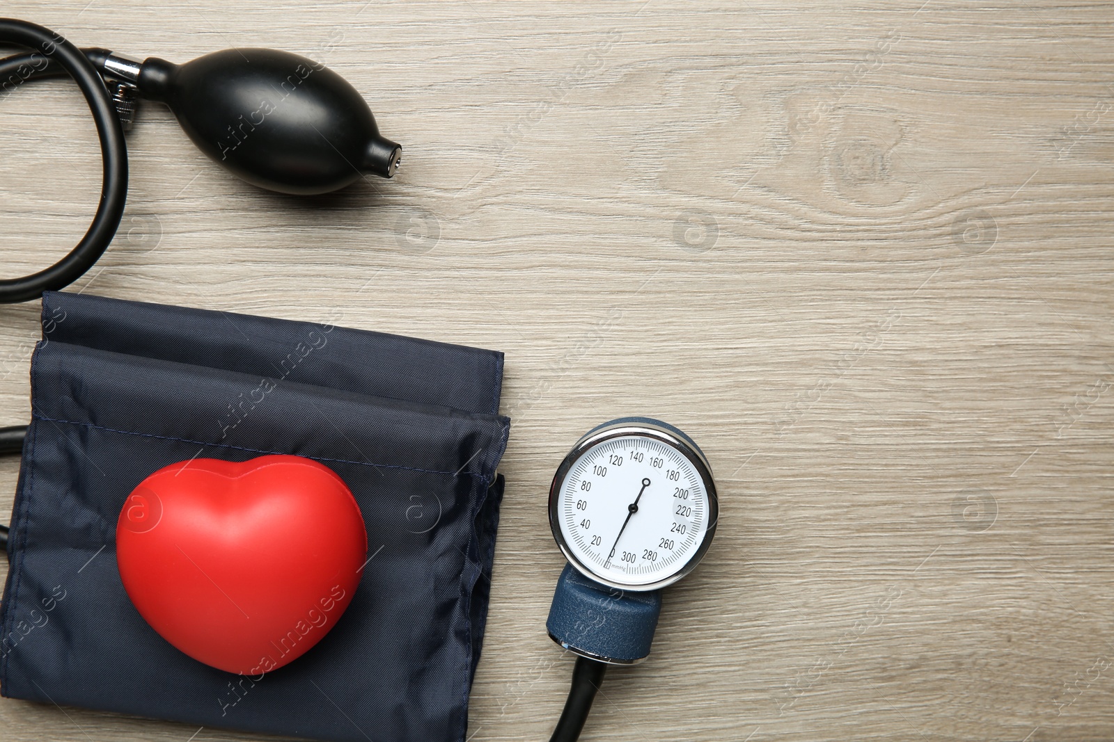 Photo of Blood pressure measuring device and squeeze heart on wooden table, top view