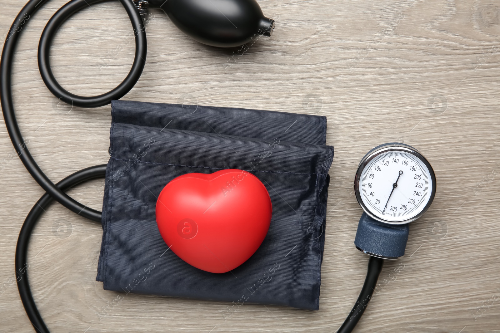 Photo of Blood pressure measuring device and squeeze heart on wooden table, top view