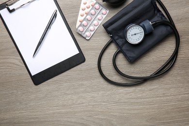 Photo of Blood pressure measuring device, pills and clipboard on wooden table, top view