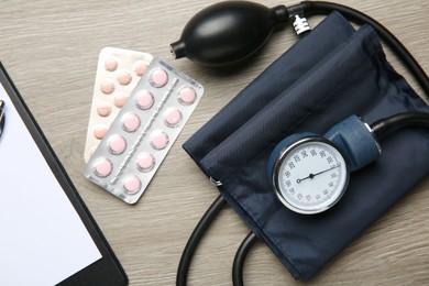 Blood pressure measuring device, pills and clipboard on wooden table, top view