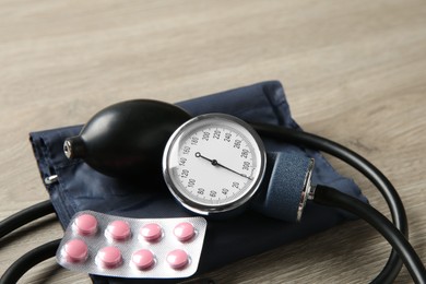 Blood pressure measuring device and pills on wooden table, closeup