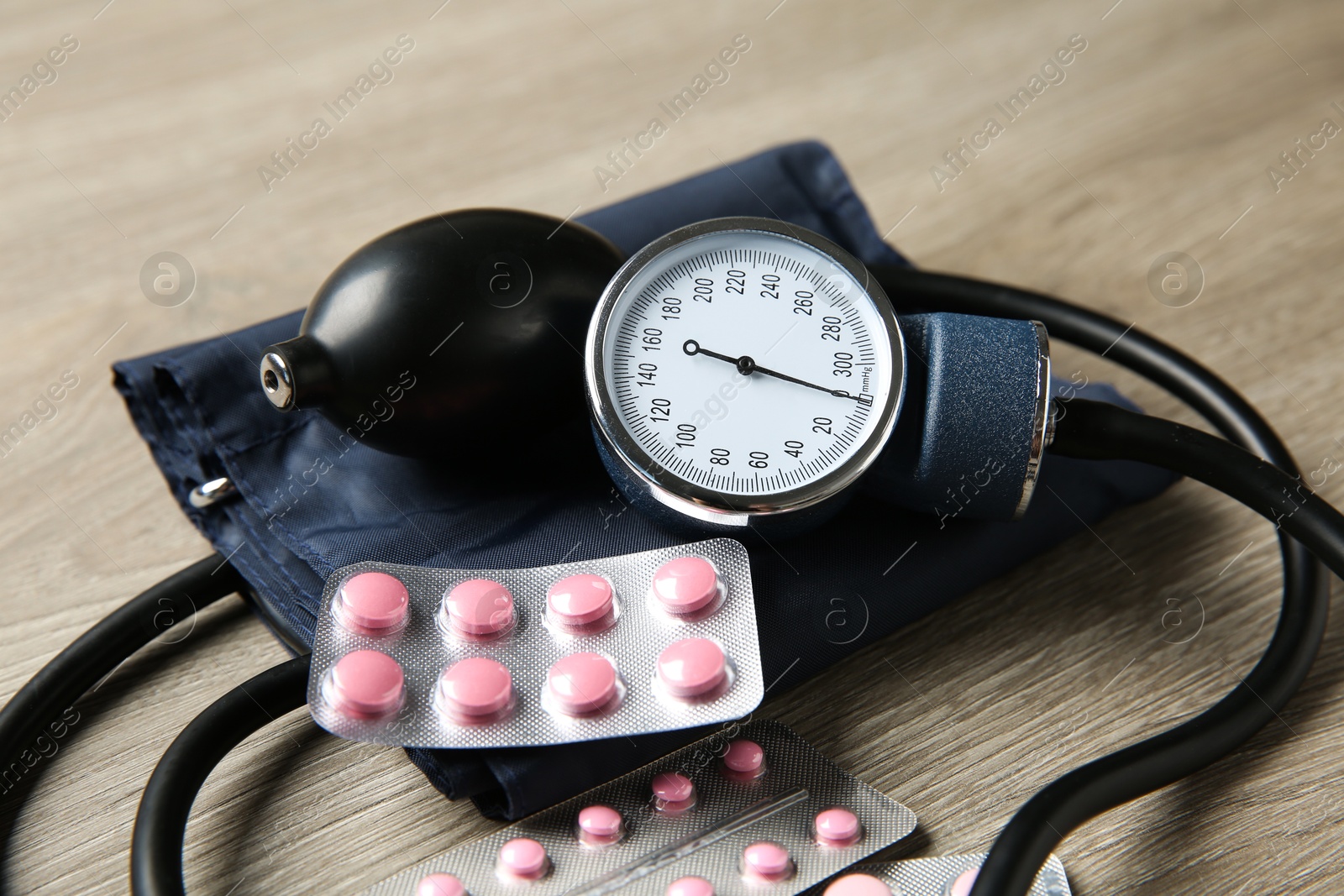 Photo of Blood pressure measuring device and pills on wooden table, closeup