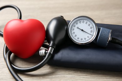 Photo of Blood pressure measuring device and squeeze heart on wooden table, closeup