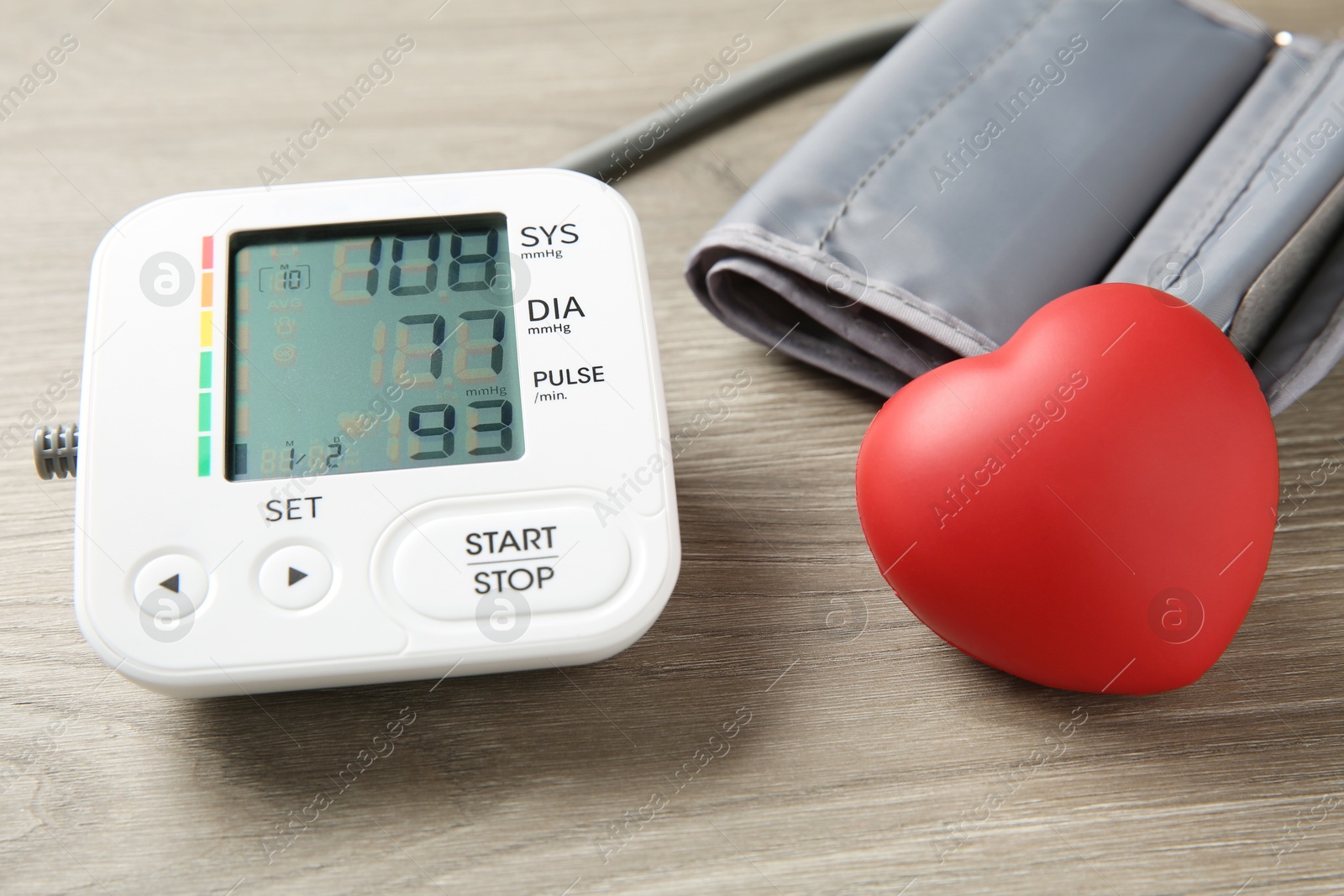 Photo of Blood pressure measuring device and squeeze heart on wooden table, closeup