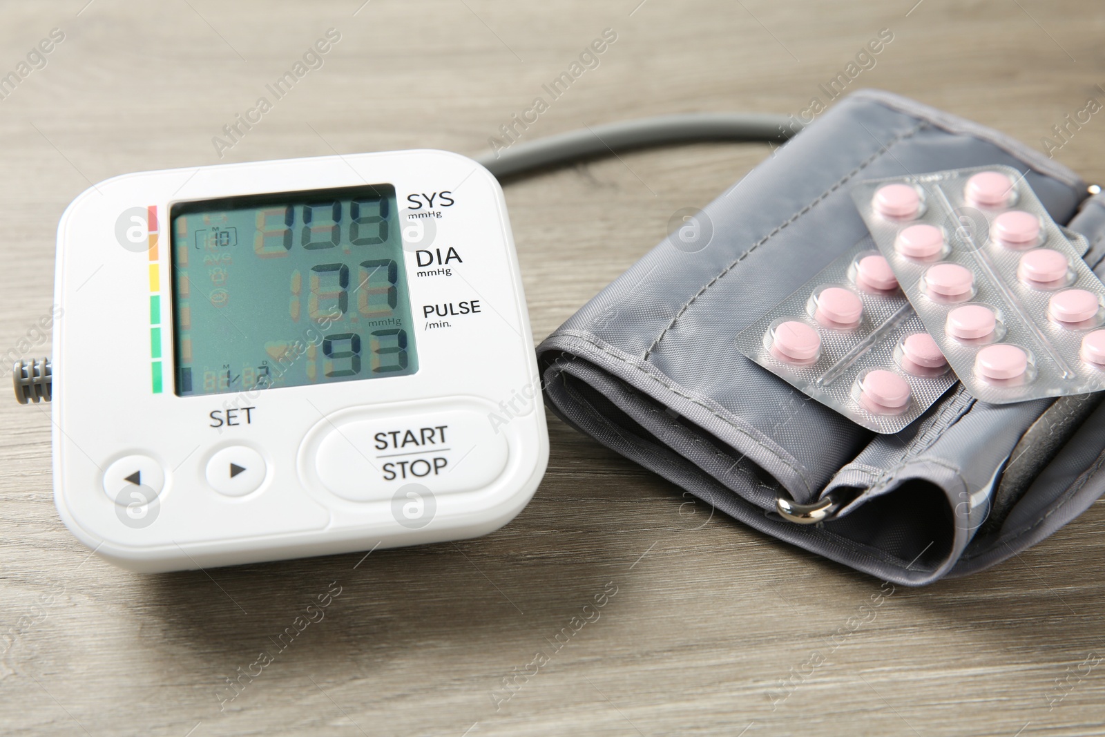 Photo of Blood pressure measuring device and pills on wooden table, closeup