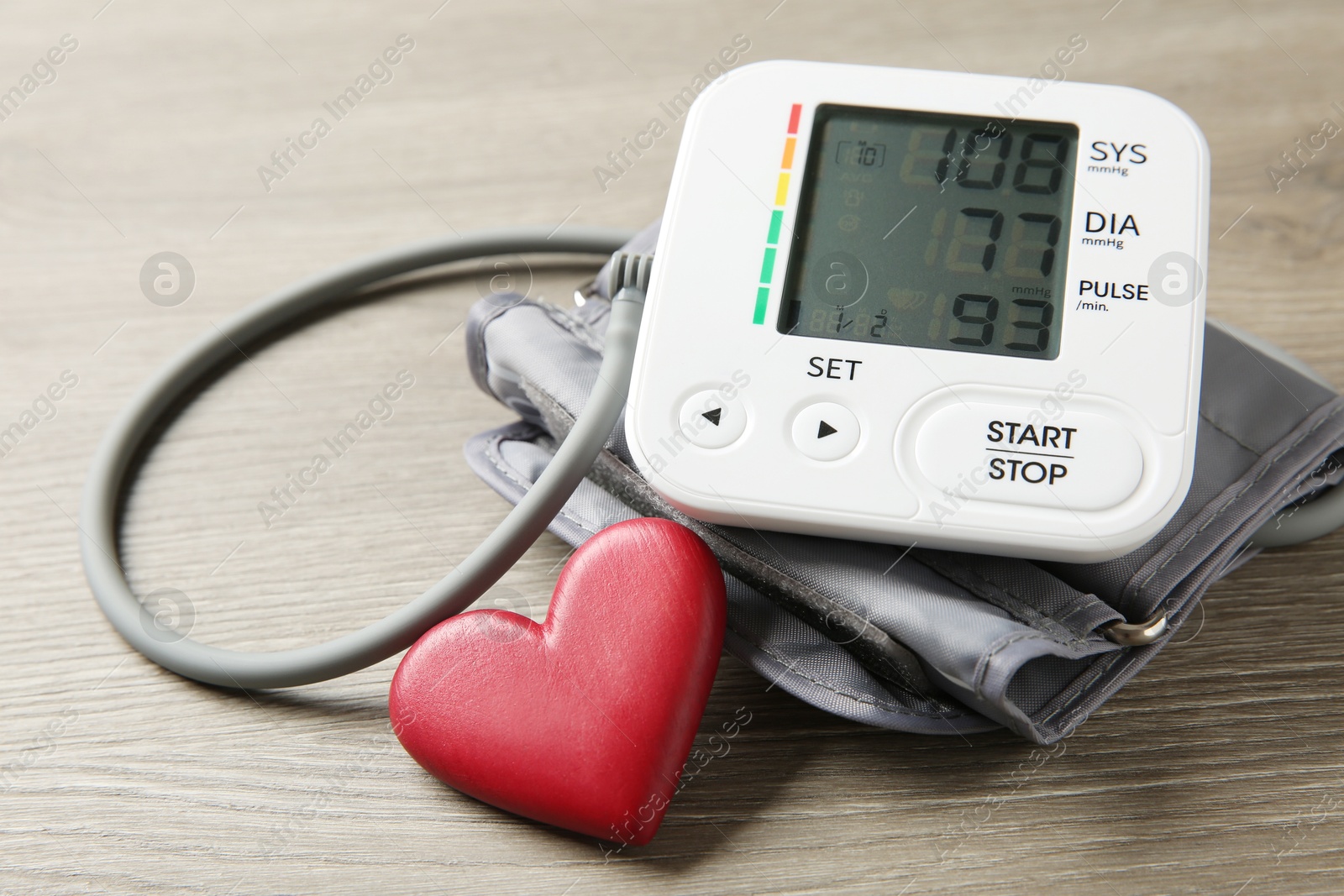 Photo of Blood pressure measuring device and heart figure on wooden table, closeup