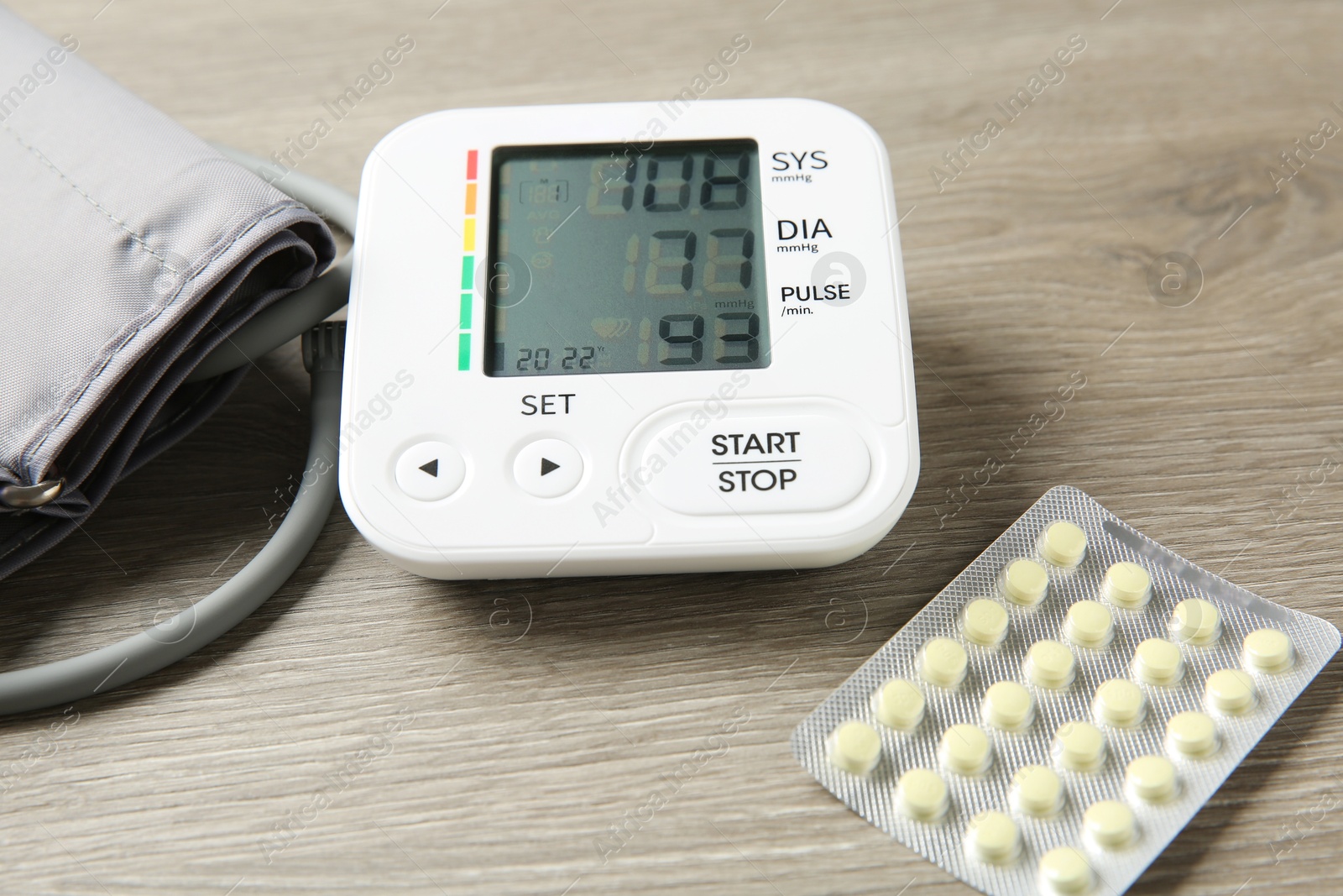 Photo of Blood pressure measuring device and pills on wooden table, closeup