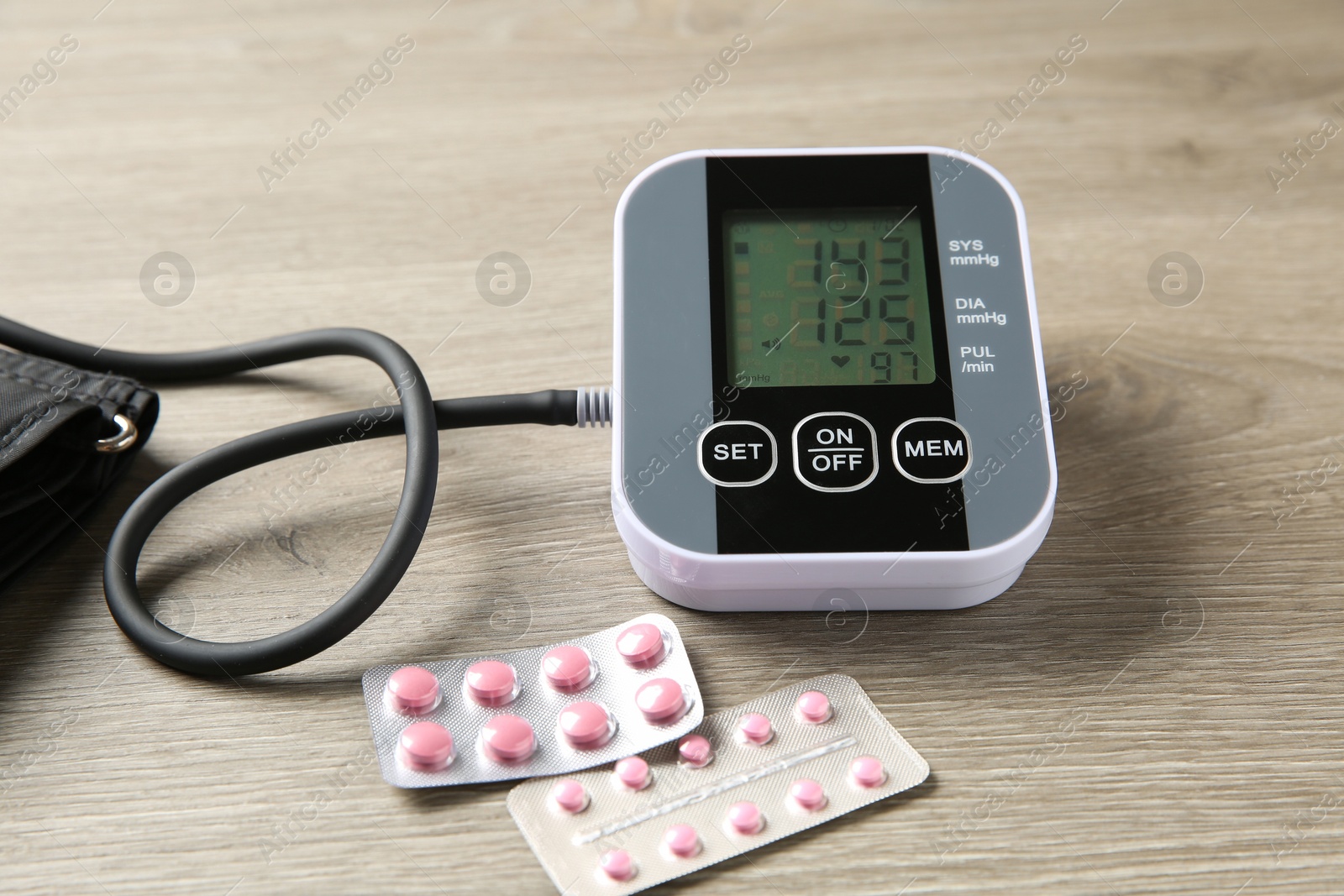 Photo of Blood pressure measuring device and pills on wooden table, closeup