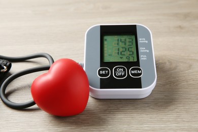 Photo of Blood pressure measuring device and squeeze heart on wooden table, closeup