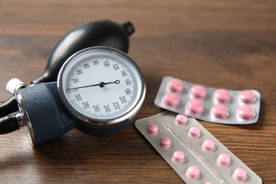 Photo of Blood pressure measuring device and pills on wooden table, closeup