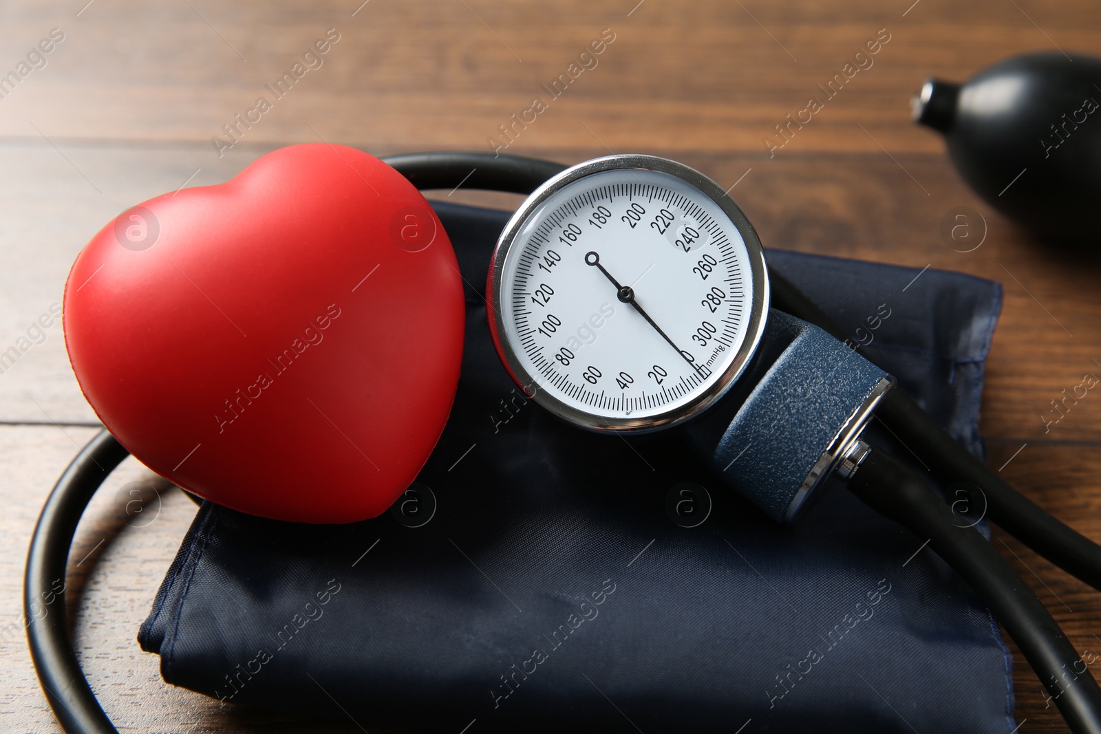 Photo of Blood pressure measuring device and squeeze heart on wooden table, closeup