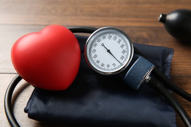 Photo of Blood pressure measuring device and squeeze heart on wooden table, closeup