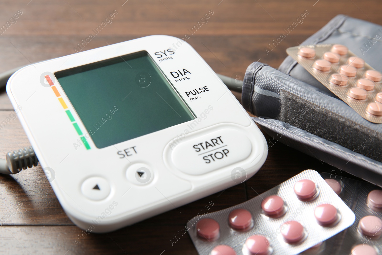 Photo of Blood pressure measuring device and pills on wooden table, closeup