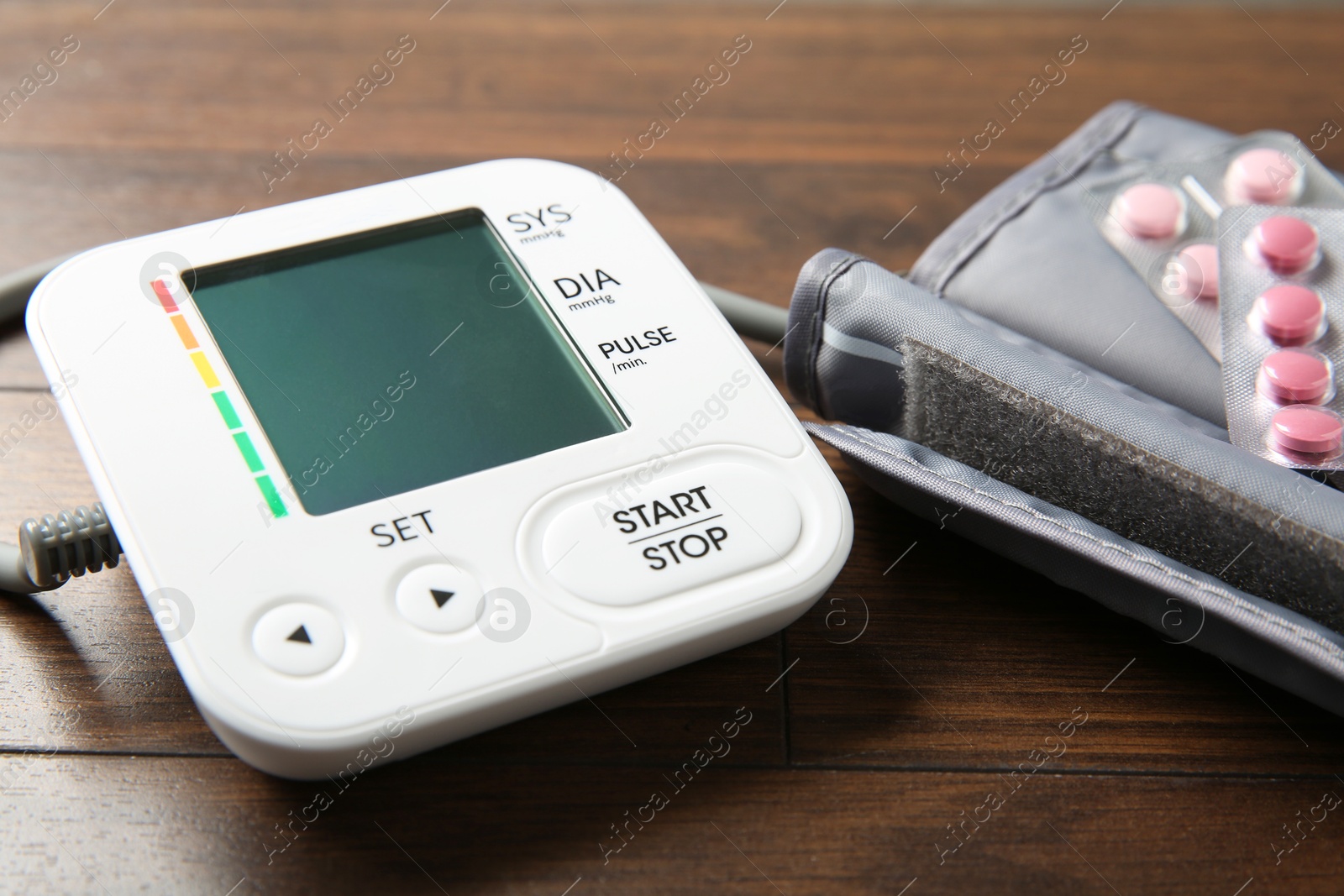 Photo of Blood pressure measuring device and pills on wooden table, closeup