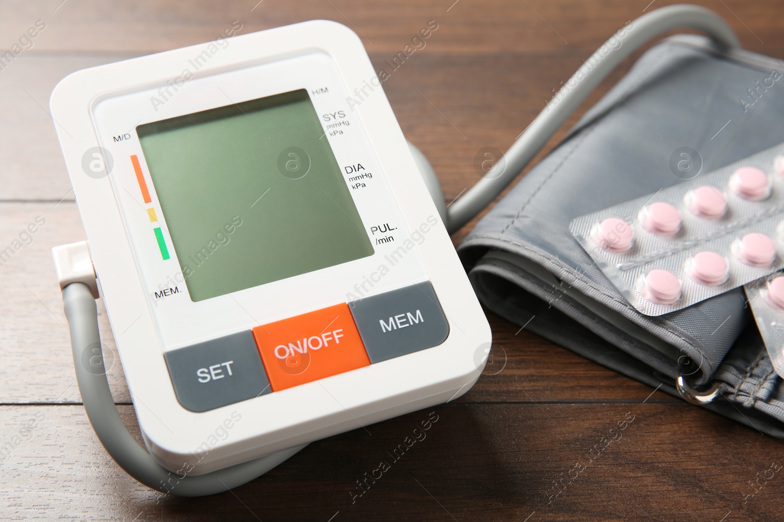 Photo of Blood pressure measuring device and pills on wooden table, closeup