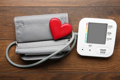 Photo of Blood pressure measuring device and heart figure on wooden table, top view